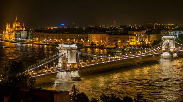 Lanțul Podului iluminat noaptea, traversând râul Dunărea în Budapesta, cu clădirile orașului în fundal.
