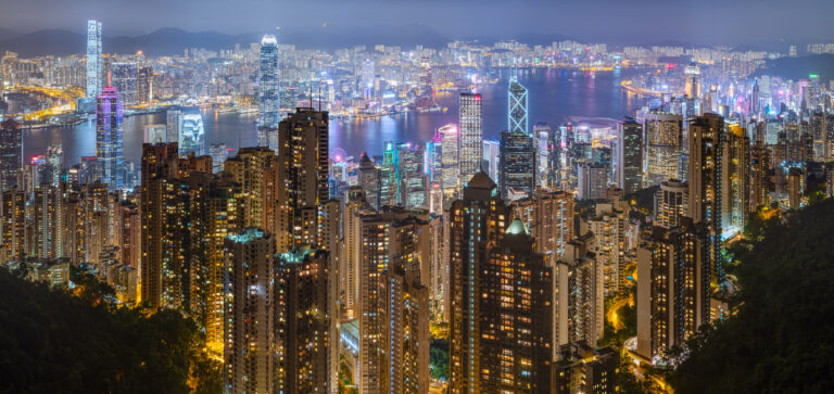 Vista notturna spettacolare di Victoria Harbour a Hong Kong con edifici moderni illuminati e acqua brillante.