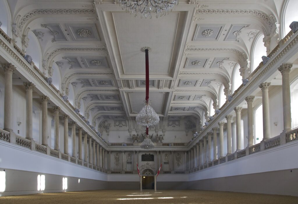 Interno della Scuola di Equitazione Spagnola a Vienna, con illuminazione naturale e dettagli architettonici spettacolari.