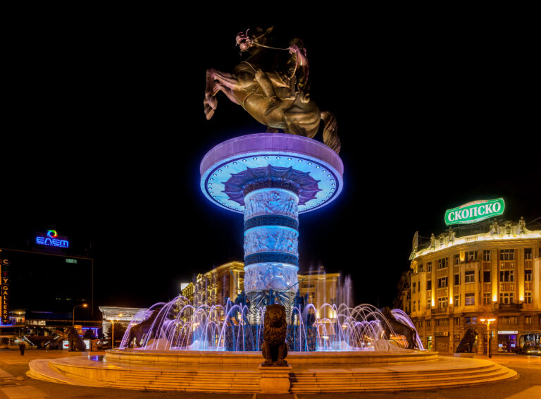 Statua equestre di Skopje illuminata di notte con la fontana in primo piano.