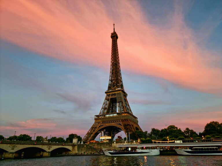 Turnul Eiffel în Paris la apus, cer roz și Sena în prim-plan.